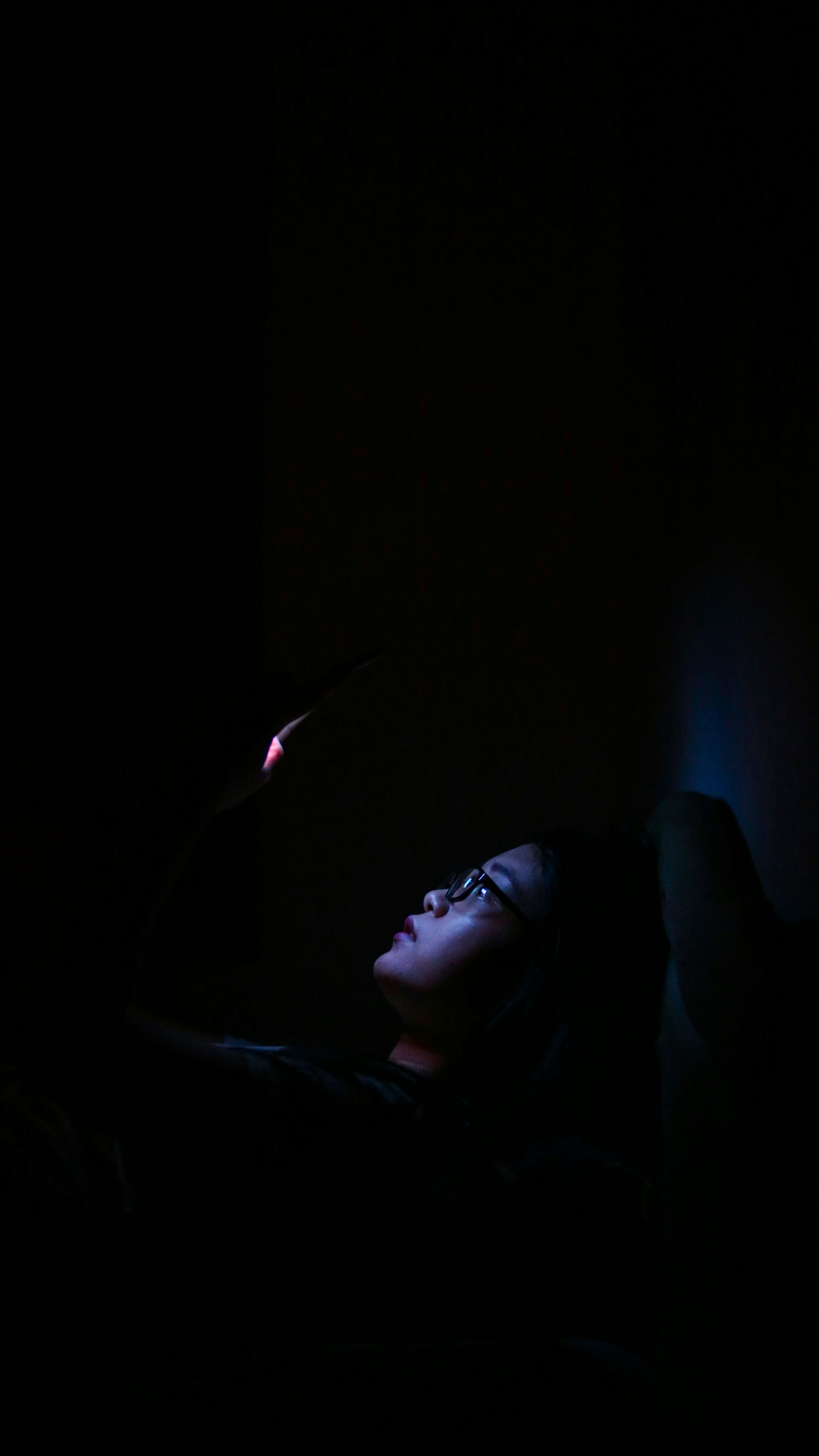 A phone face-down on a nightstand, screen-light leaking