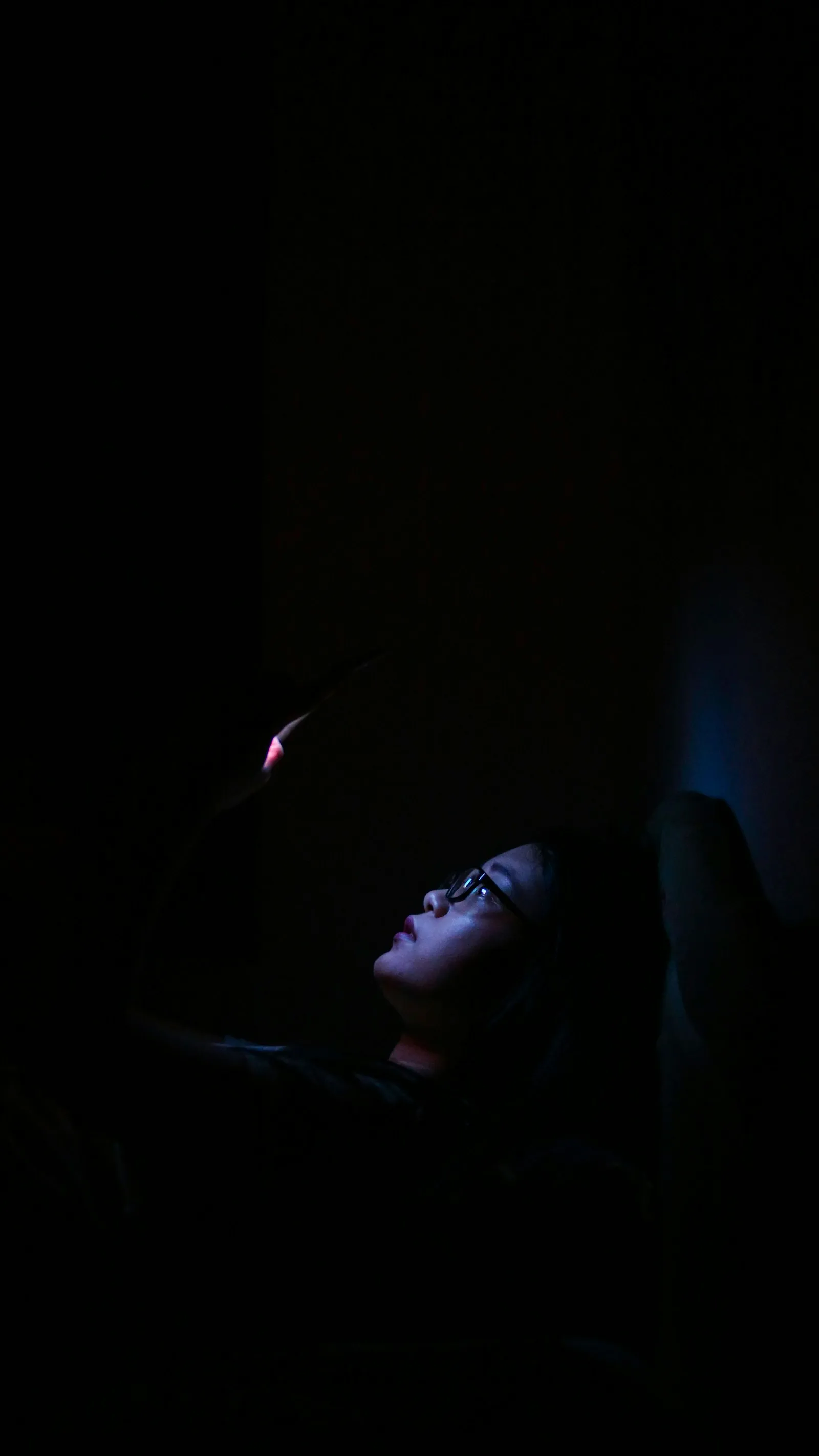 A phone face-down on a nightstand, screen-light leaking